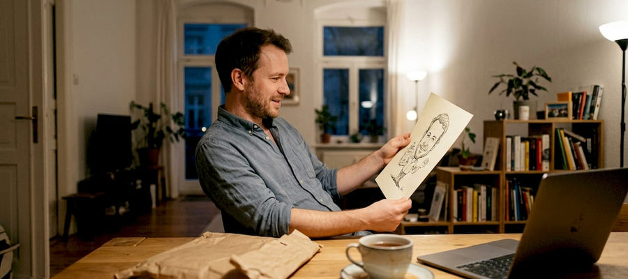 Ein Mann begutachtet eine Karikatur am Wohnzimmertisch.