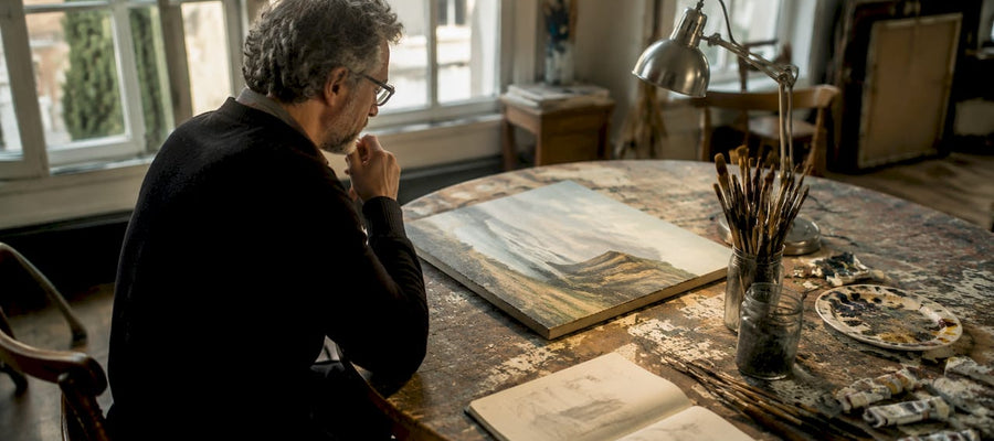 Ein Mann steht im Atelier und vertieft sich in die Betrachtung eines Gemäldes.