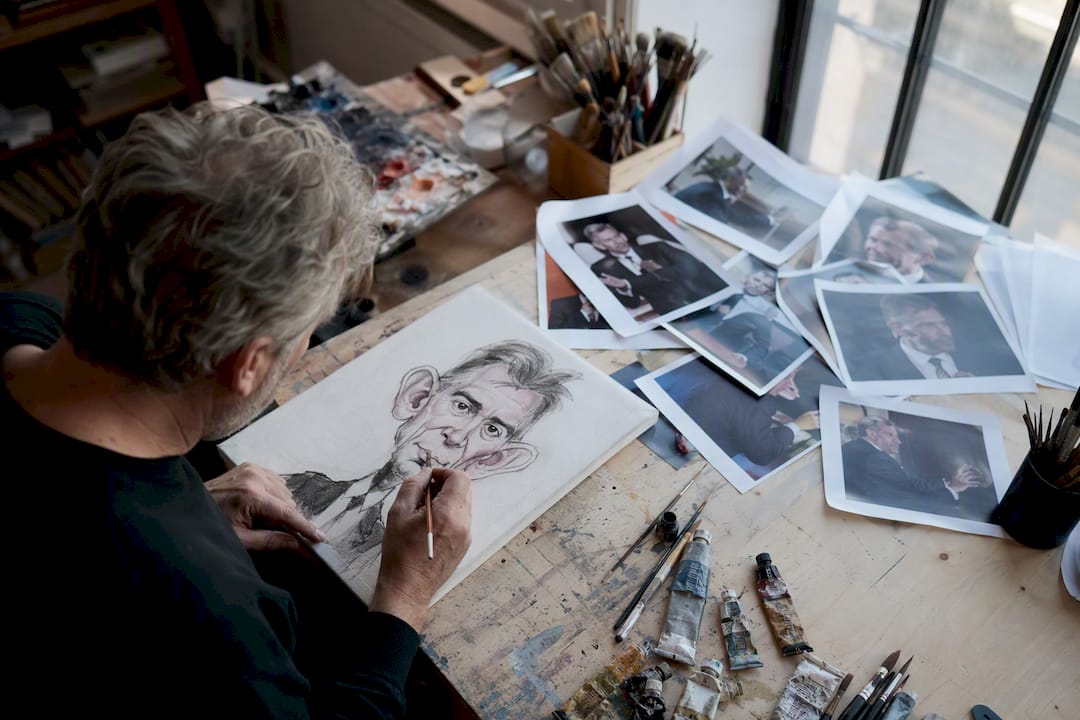 Künstler zeichnet Karikatur anhand mehrerer Fotos